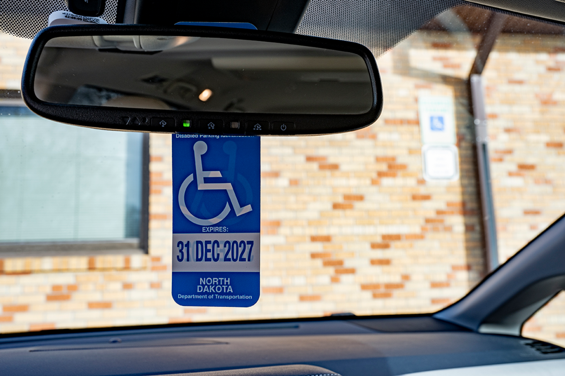 A disabled parking permit hangs from the front mirror of a car.