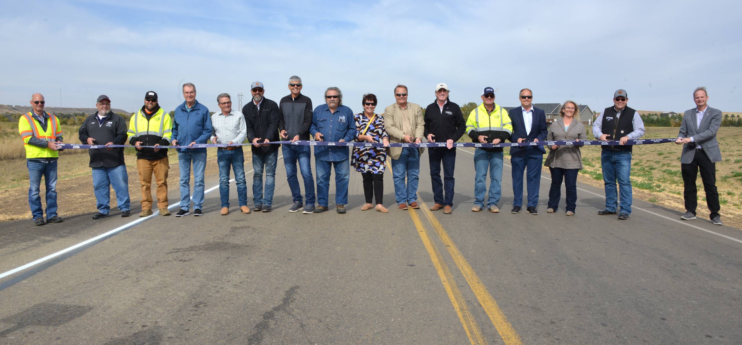 16 people stand across a highway with a blue ribbon stretched between them