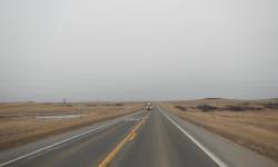 A portion of the US 85 two lane highway with oncoming traffic. Sky is gray with dry grass. 