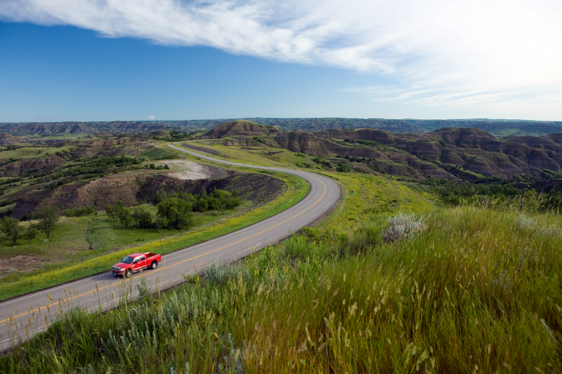 Red pickup drives on road near Theodore Roosevelt National Park in North Dakota.